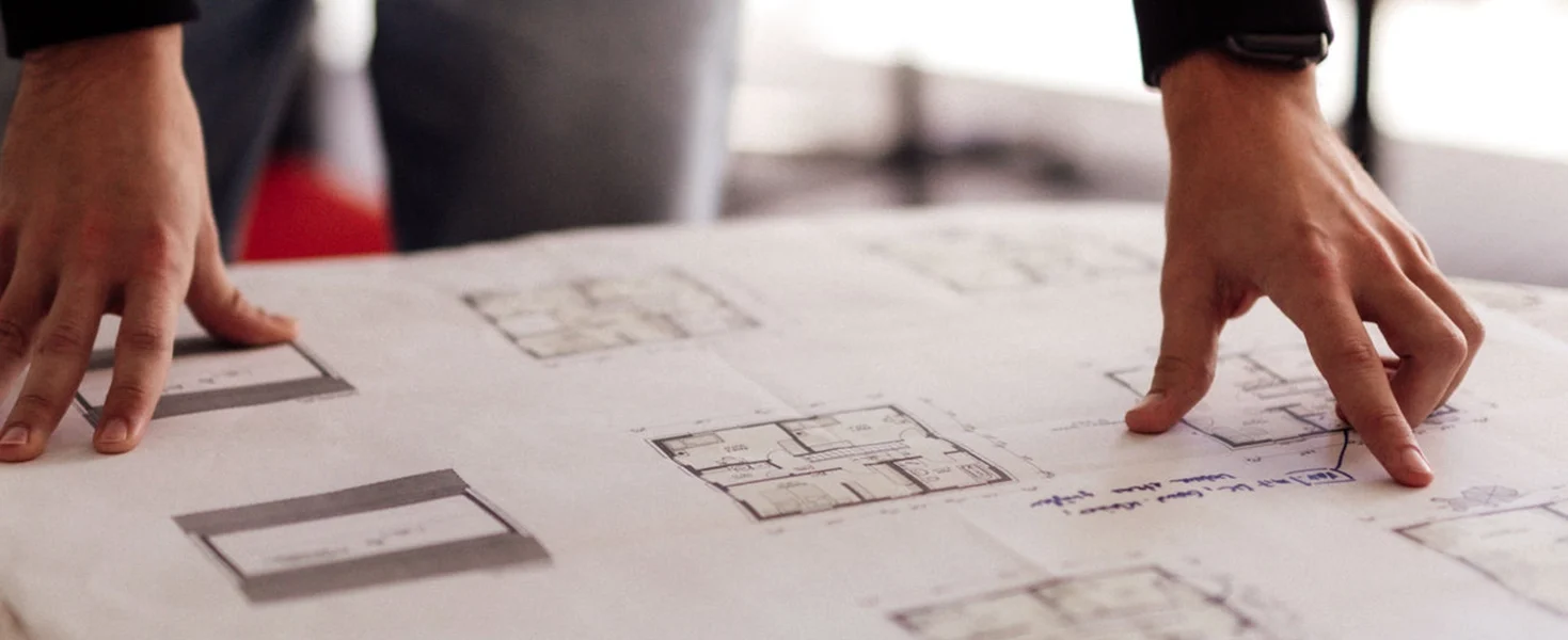 Person zeigt auf Baupläne auf einem Tisch.