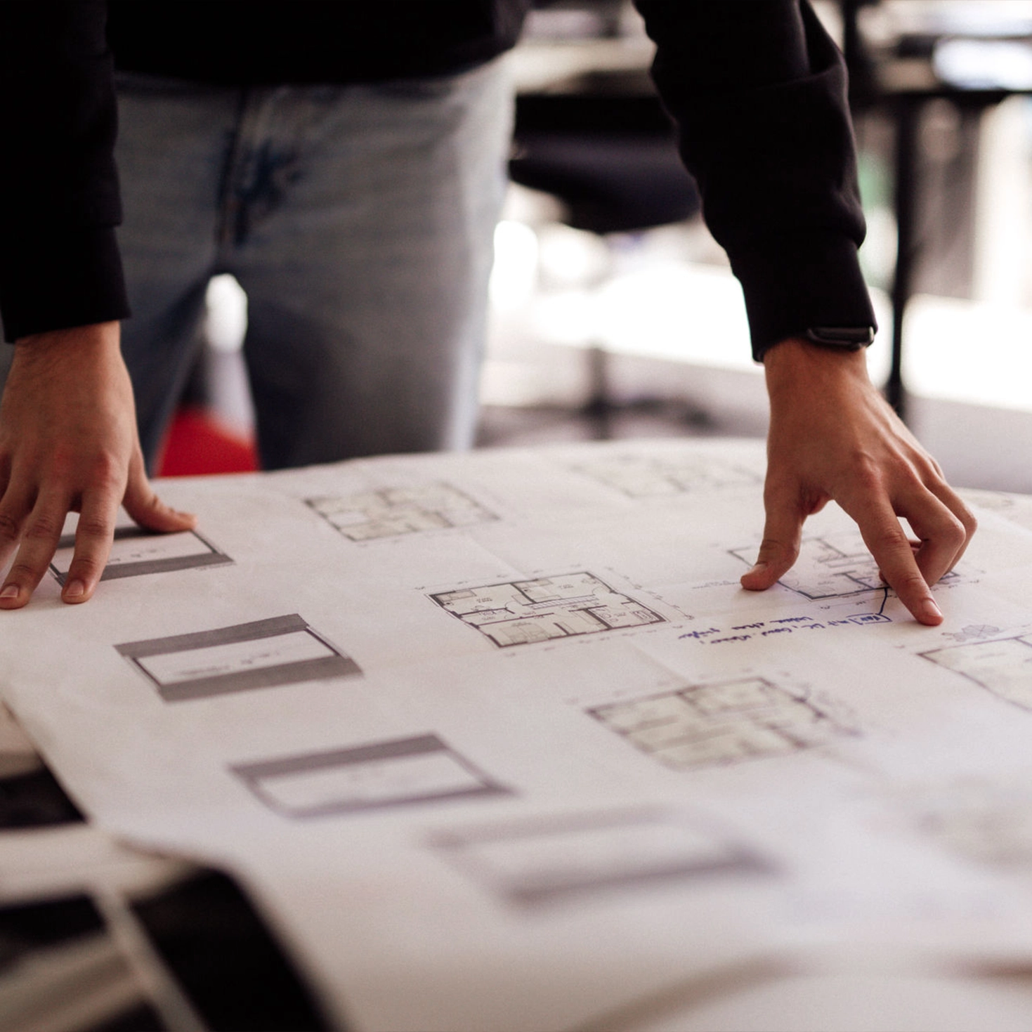 Person zeigt auf Baupläne auf einem Tisch.