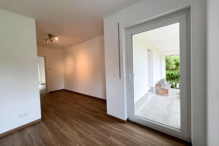 Leerer Raum mit Holzboden und Blick auf eine Terrasse.