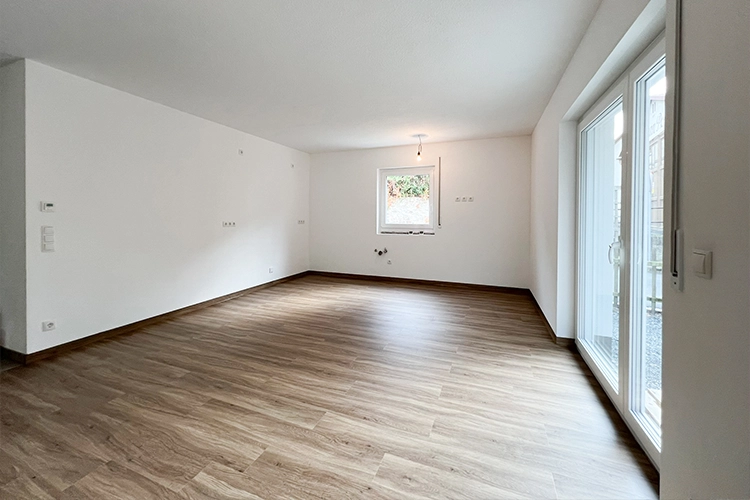 Leerer Raum mit Holzboden und großen Fenstern.