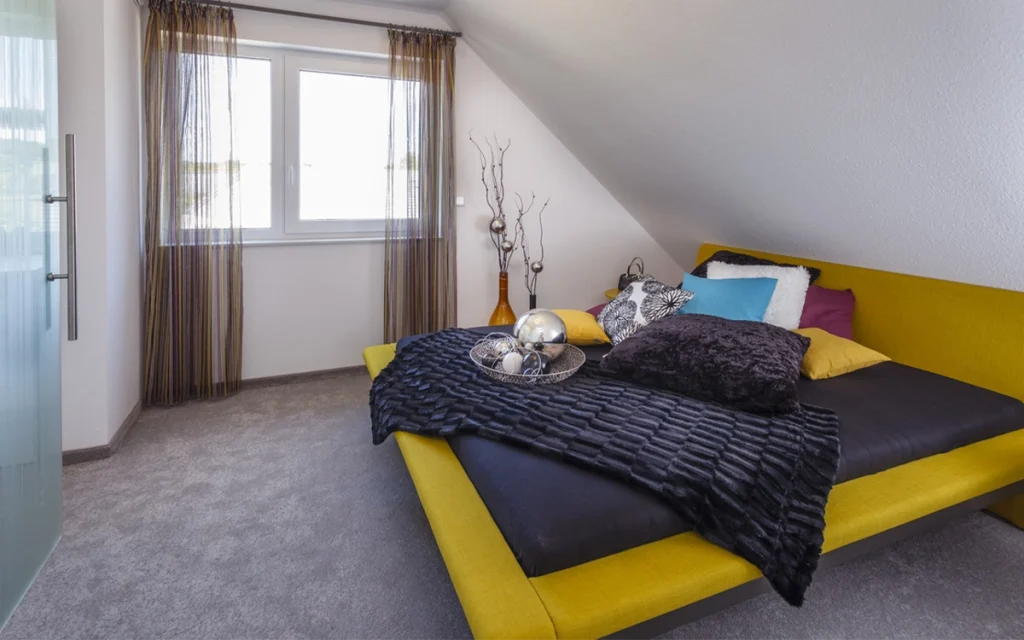 Gemütliches Schlafzimmer mit gelbem Bett und bunten Kissen.