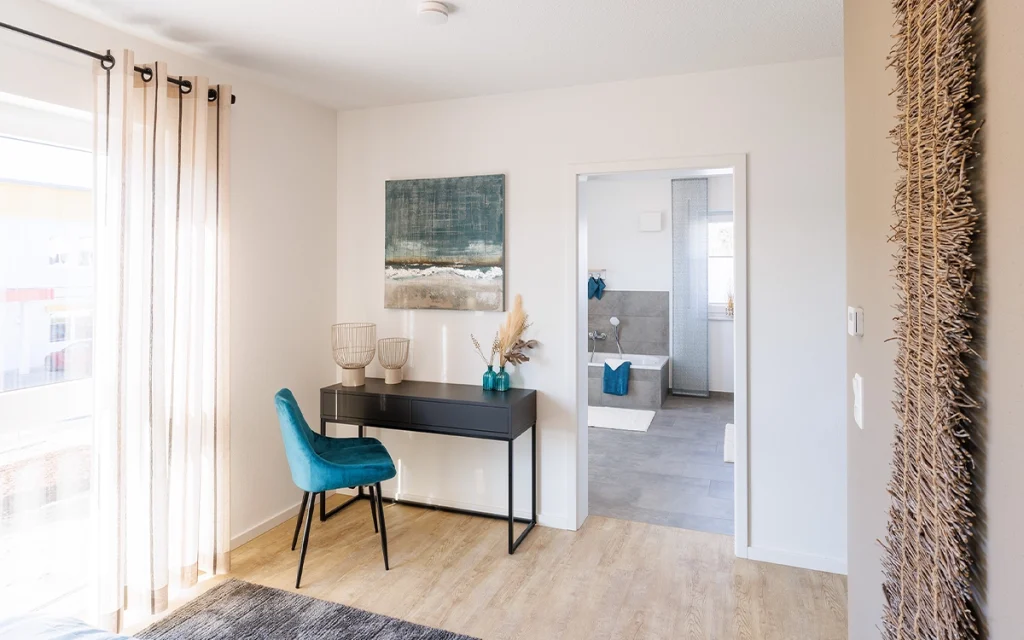 Helles Zimmer mit Schreibtisch und blauem Stuhl.