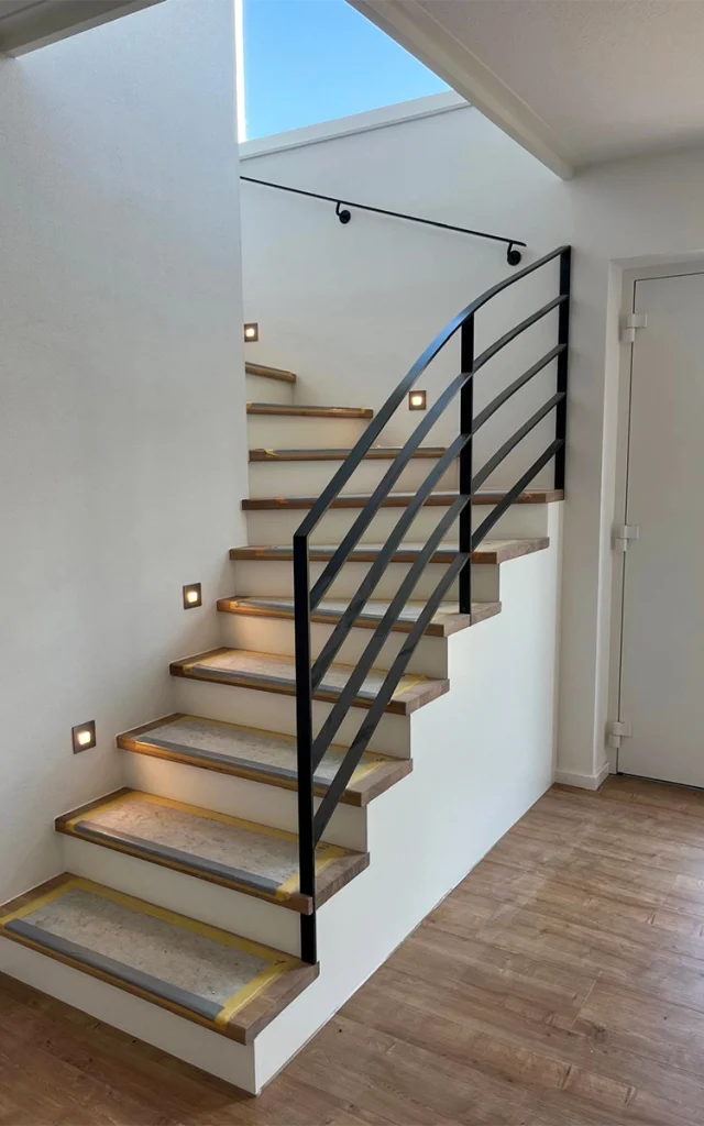 Treppe mit schwarzem Geländer und Beleuchtung.