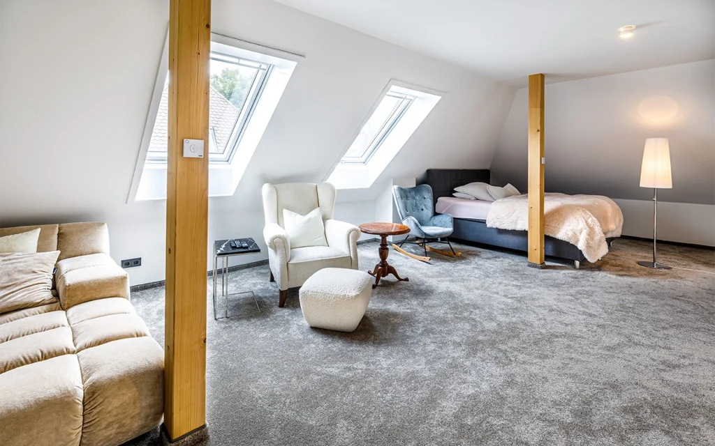 Großzügiges Dachzimmer mit Sofa, Sessel und Bett.