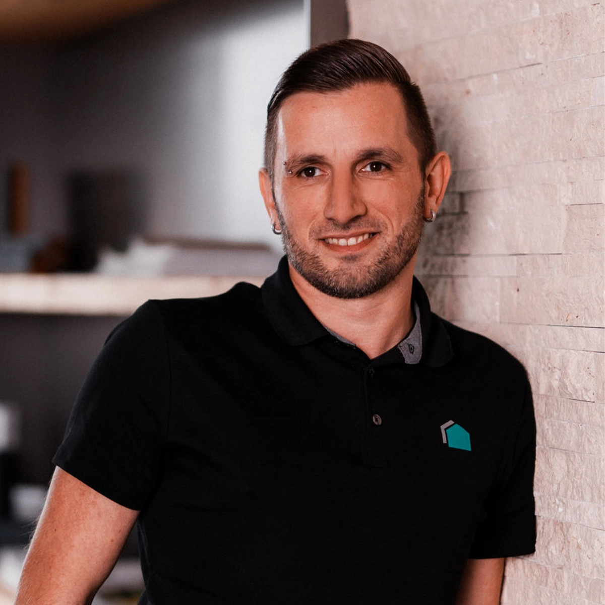 Alexander lehnt an einer Wand und lächelt in die Kamera.