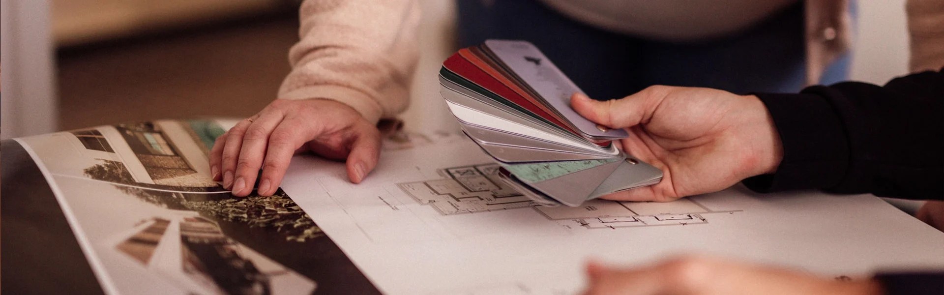 Personen betrachten Farbmuster über Bauplänen.