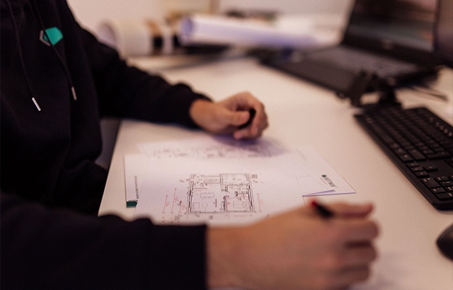 Person am Schreibtisch mit Bauplänen.