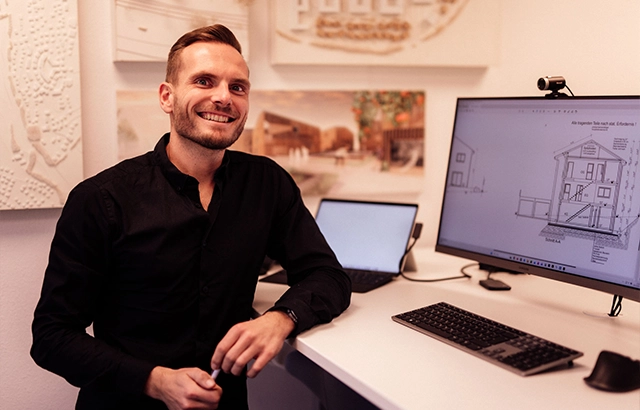Dominik in seinem Büro vor einem Computer mit Bauplan.
