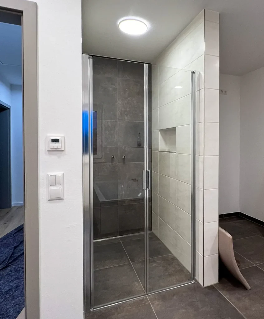 Moderne Dusche mit Glastür und grauen Fliesen.