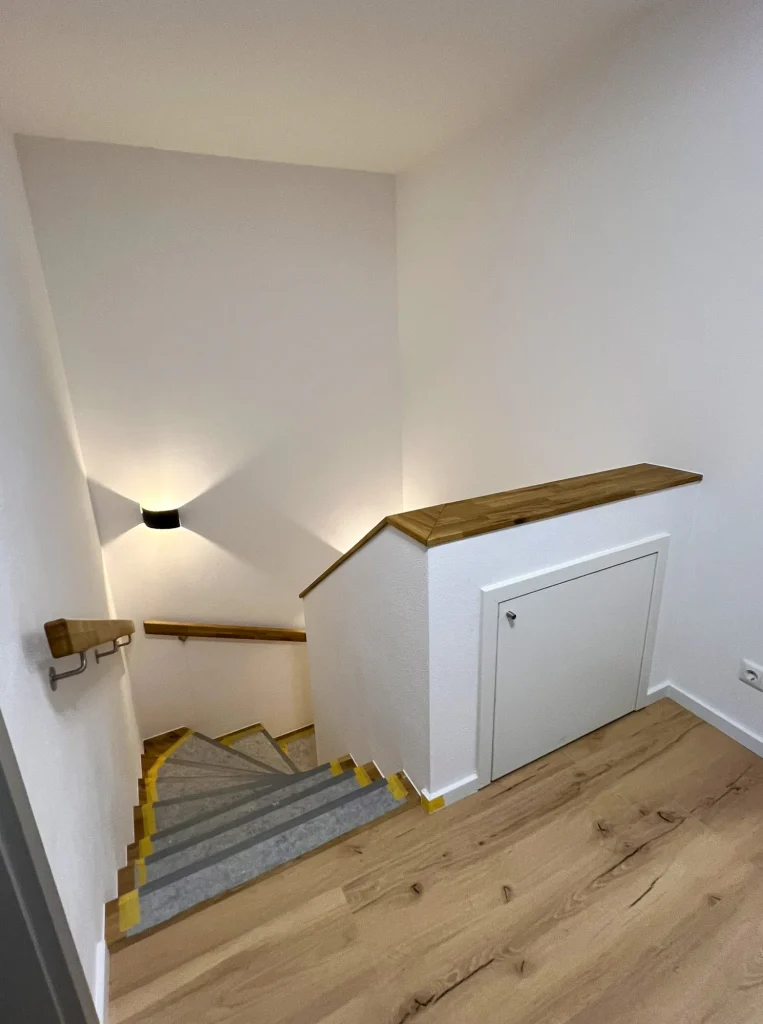 Treppe mit Wandbeleuchtung und Holzgeländer.