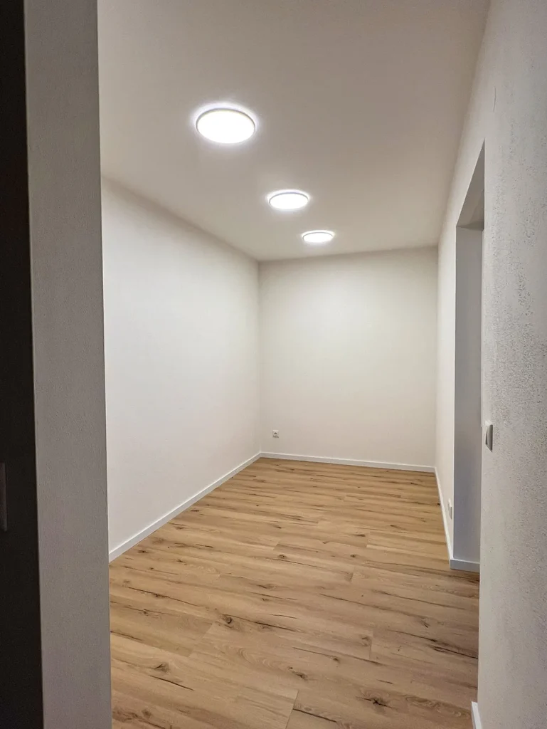 Leerer Raum mit Holzboden und Deckenleuchten.