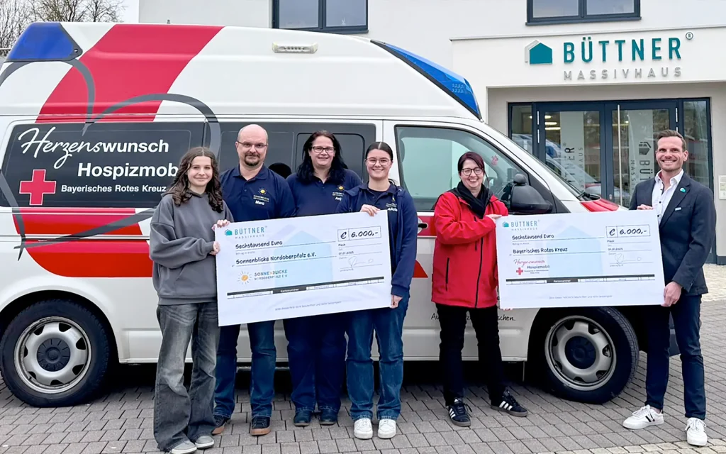 Personen halten große Schecks vor einem Krankenwagen.