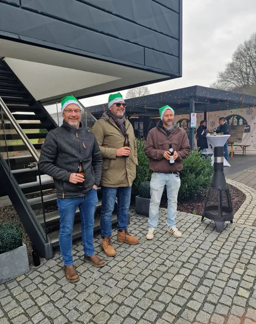 Drei Personen mit Mützen stehen draußen und halten Flaschen.