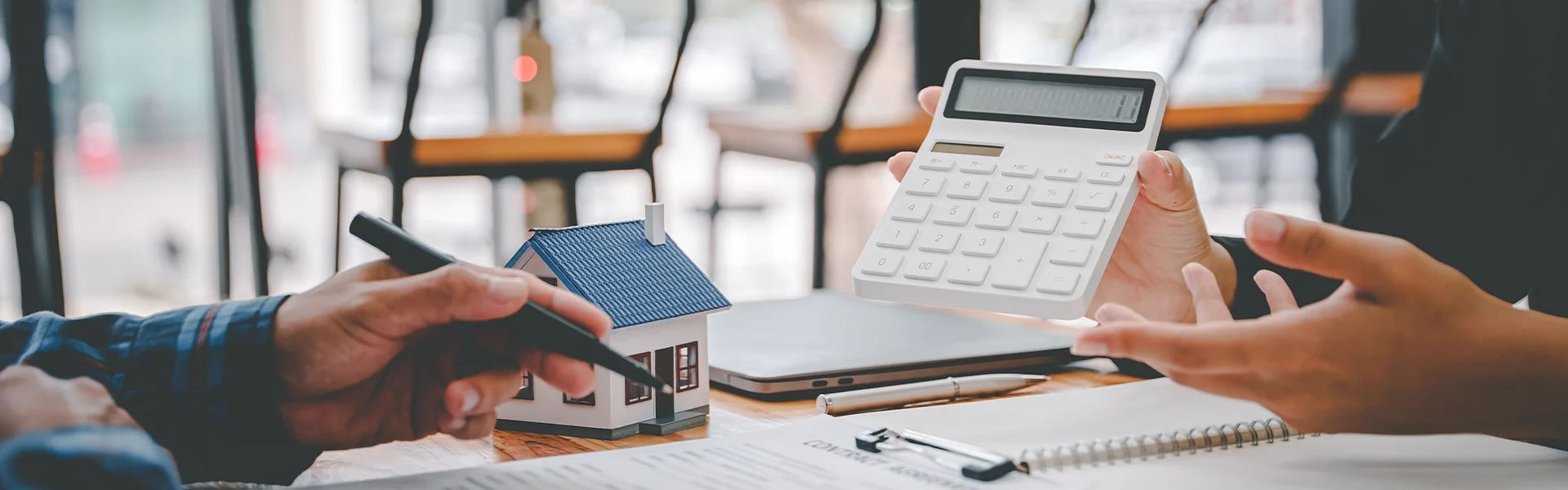 Personen diskutieren über Immobilienfinanzen mit einem Miniaturhausmodell und Taschenrechner.