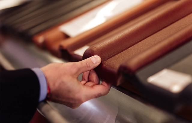 Eine Hand berührt eine Dachziegelprobe.