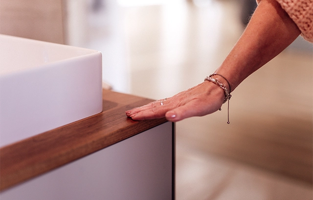 Eine Hand berührt eine hölzerne Oberfläche neben einem Waschbecken.