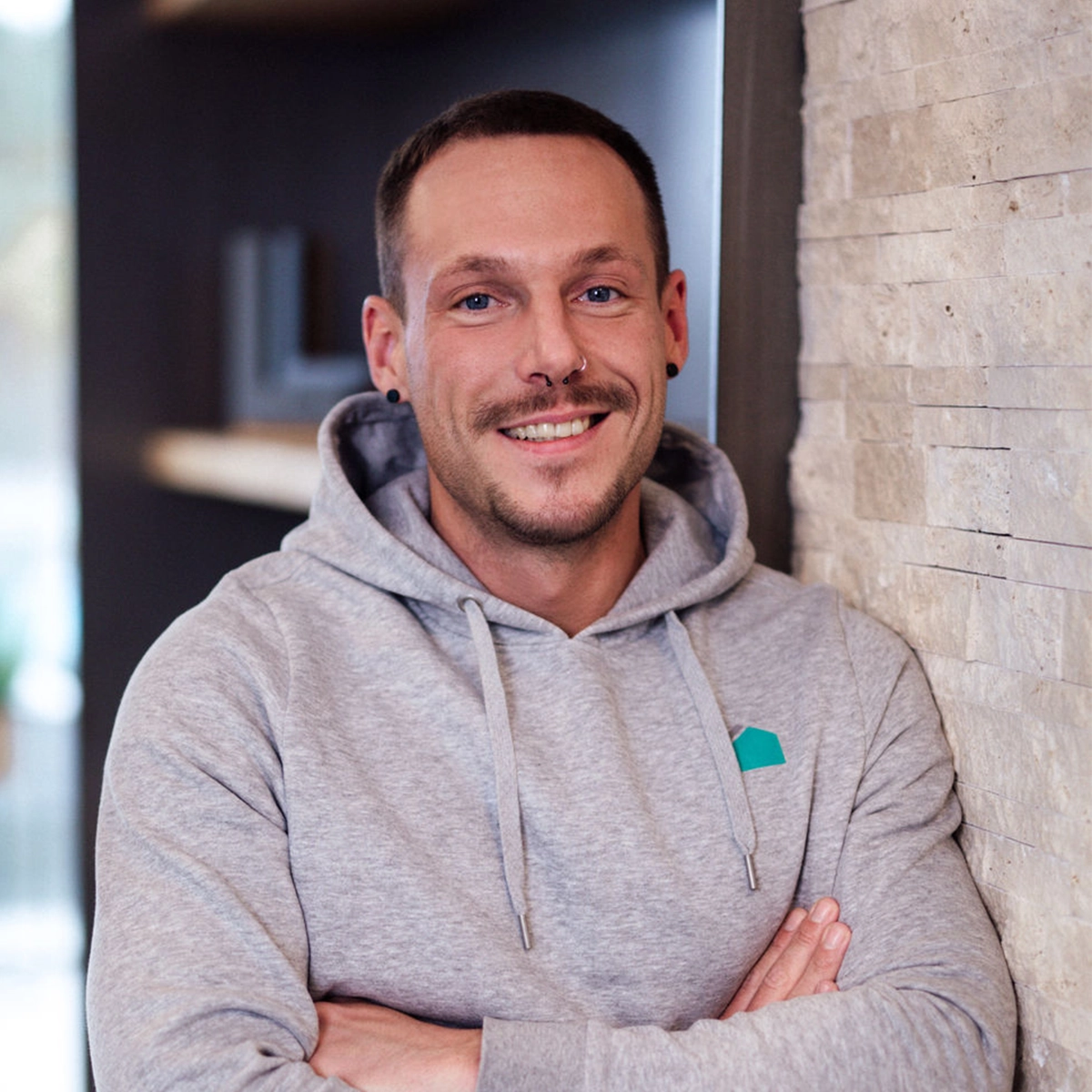 Philipp steht lächelnd in einem grauen Hoodie vor einer Wand.