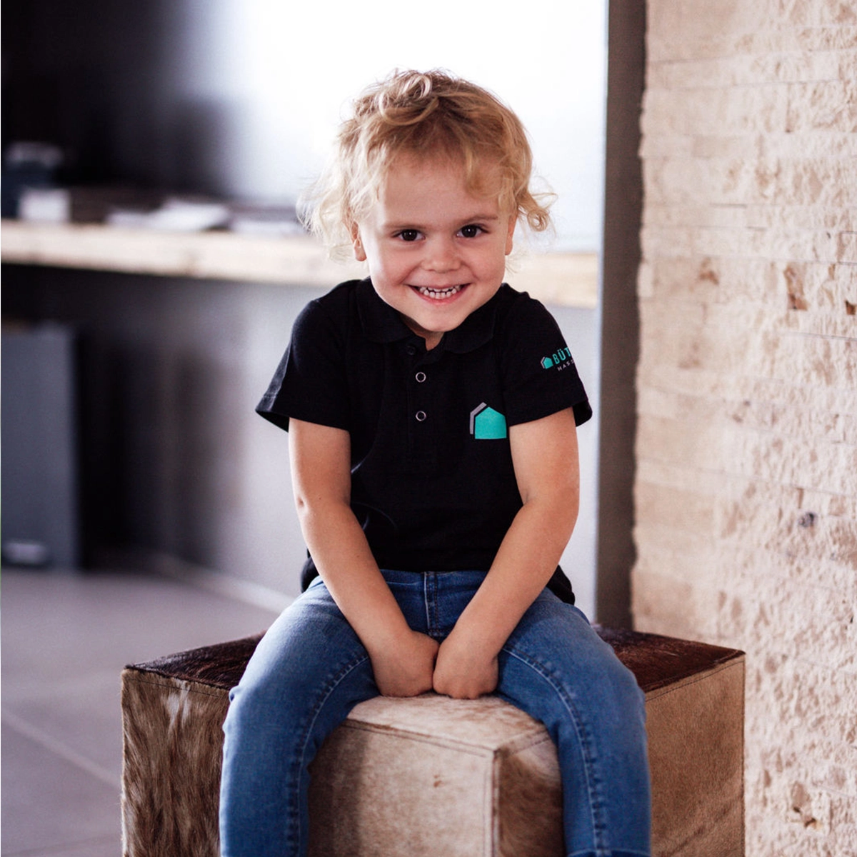 Toni sitzt auf einem Hocker und lächelt.