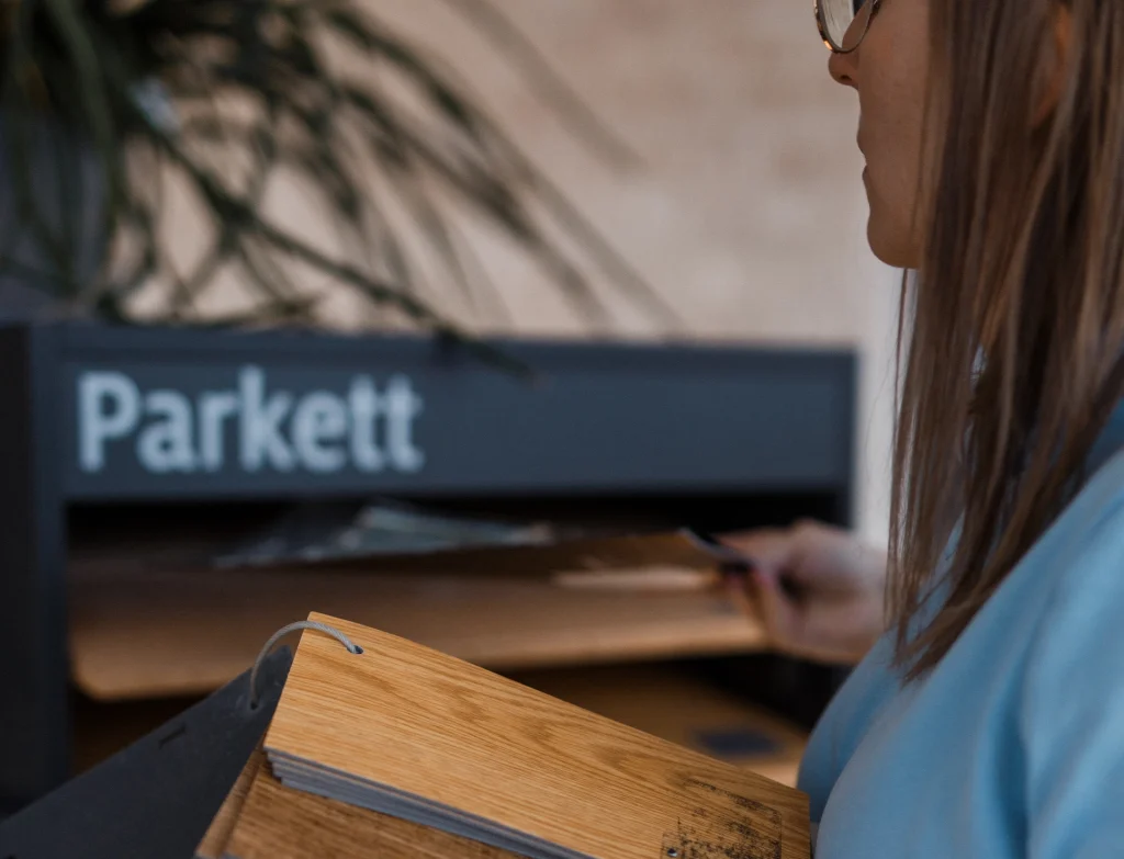 Alisa betrachtet Holzmuster vor Parkettregal.