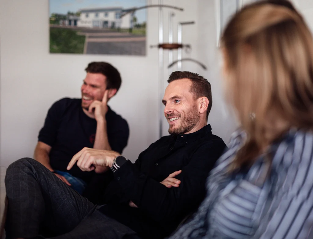Tim, Dominik und Alisa, die zusammen bei einer Besprechung lachen.