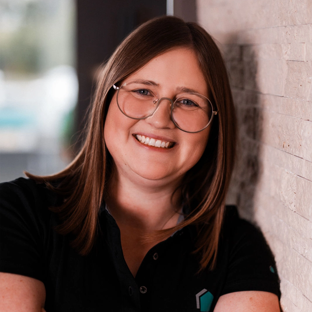 Linda lächelt vor einer Steinwand.