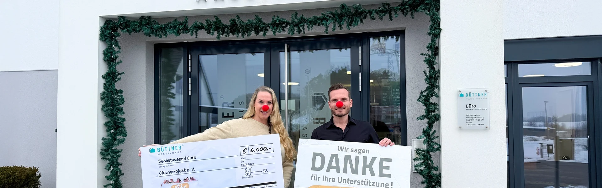 ZweiPersonen stehen vor dem Gebäude von Büttner Massivhaus und halten einen großen Spendenscheck über 6.000 Euro in die Kamera.