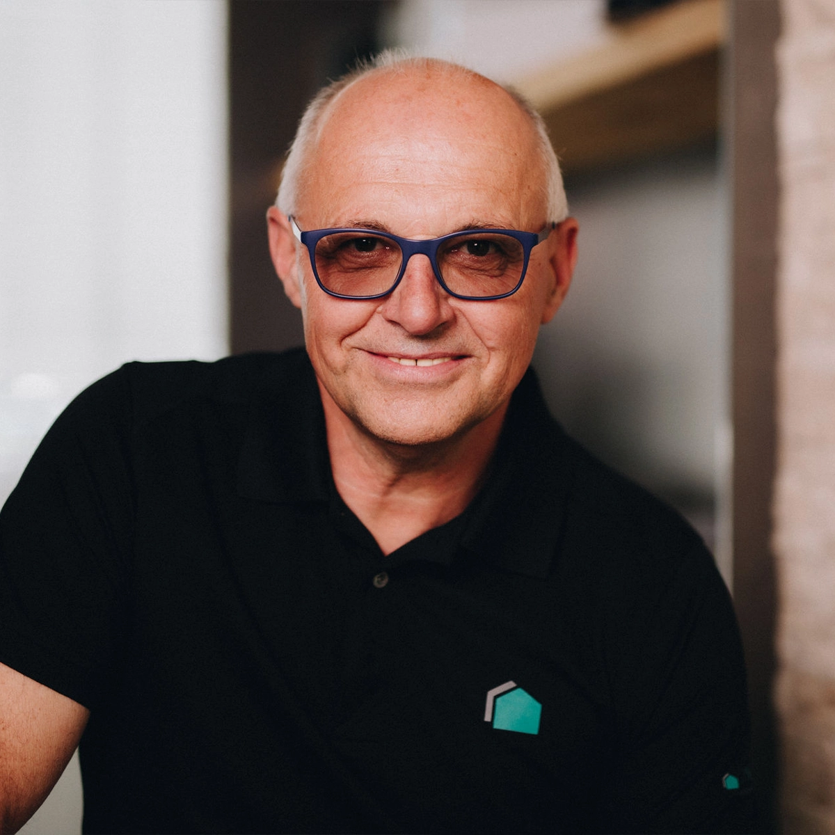 Anton lächelt freundlich in die Kamera und trägt ein schwarzes Poloshirt mit Büttner-Logo sowie eine auffällige blaue Brille.