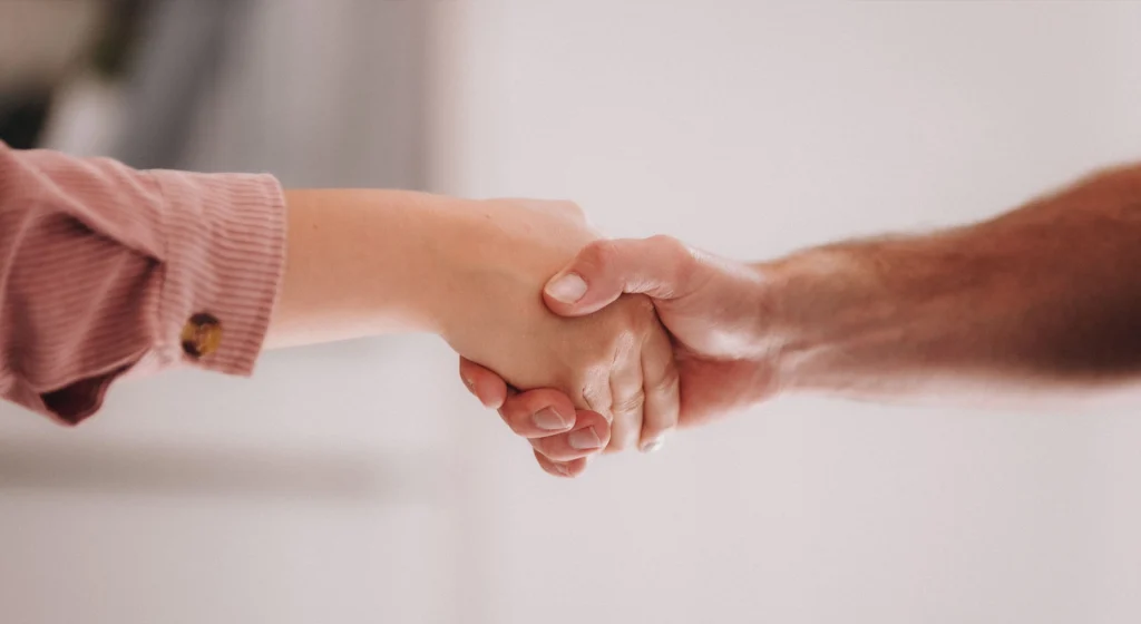 Zwei Personen geben sich die Hand als Zeichen für Vertrauen und partnerschaftliche Zusammenarbeit bei Büttner Massivhaus.
