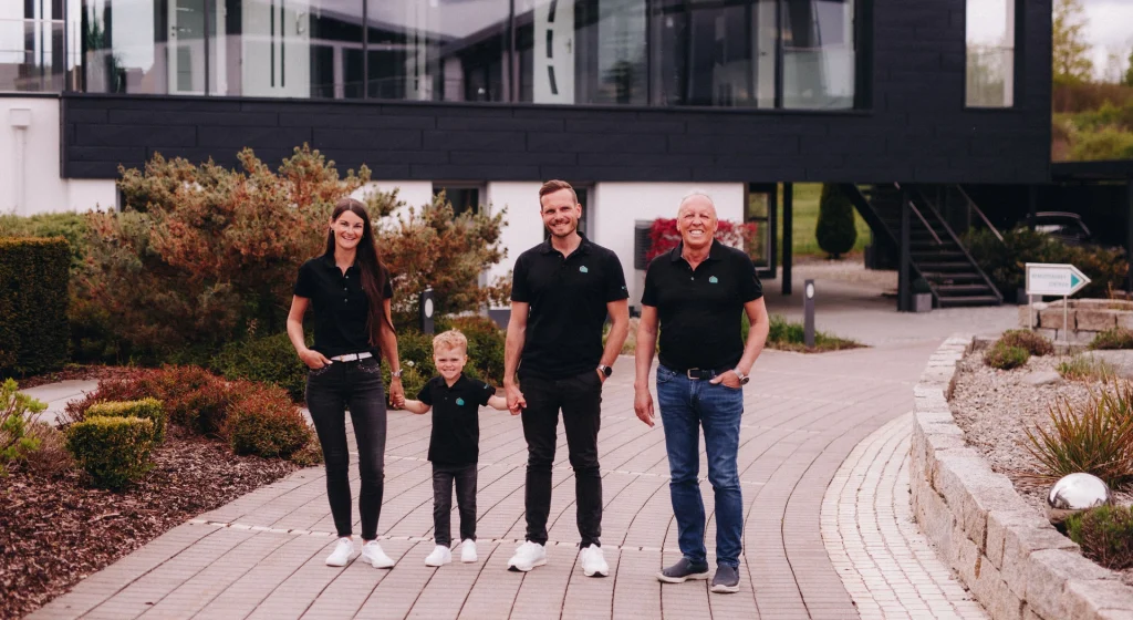 Madeleine, Ehefrau von Geschäftsführer Dominik Büttner, gemeinsam mit Sohn Toni (Junior), Dominik Büttner und Werner Büttner – Senior und ebenfalls Geschäftsführer – vor dem modernen Büttner Massivhaus.