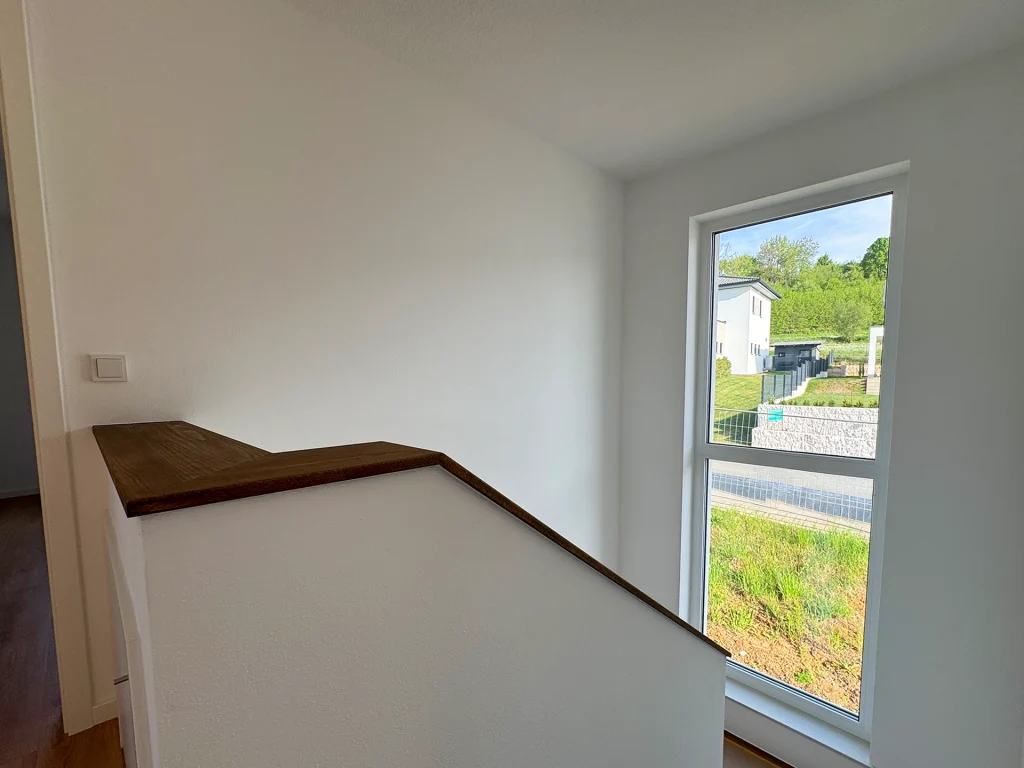 Heller Treppenaufgang mit großem Fenster und modernen Holzelementen für eine freundliche Wohnatmosphäre.