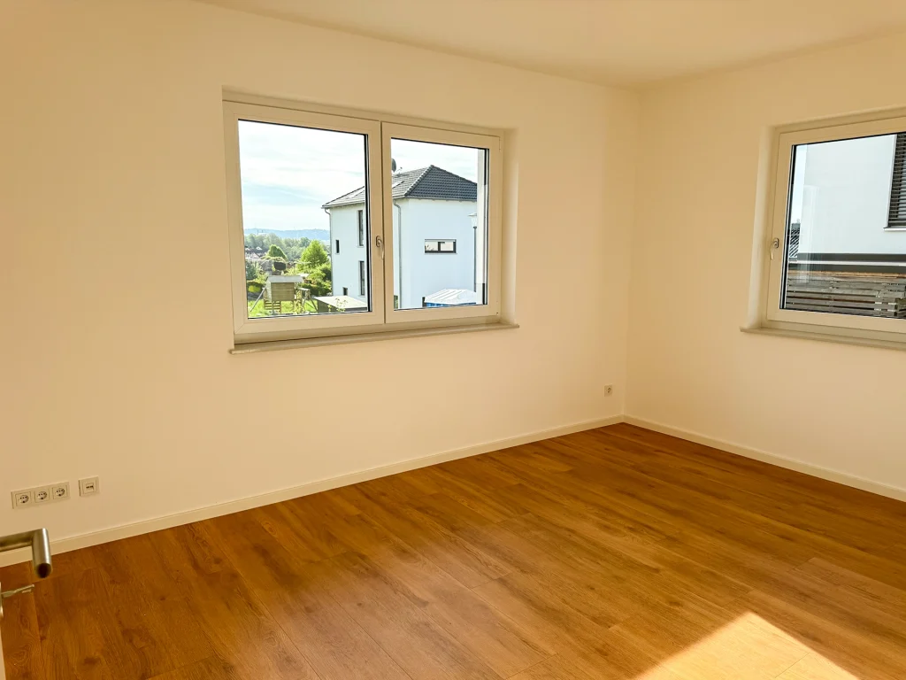 Heller Wohnraum mit großzügigen Fenstern und warmem Vinylboden in Echtholzoptik.