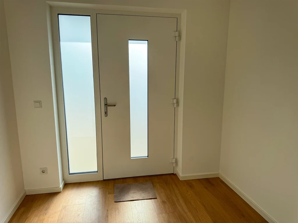 Moderner Eingangsbereich mit großzügigen Glaselementen und heller, einladender Atmosphäre.