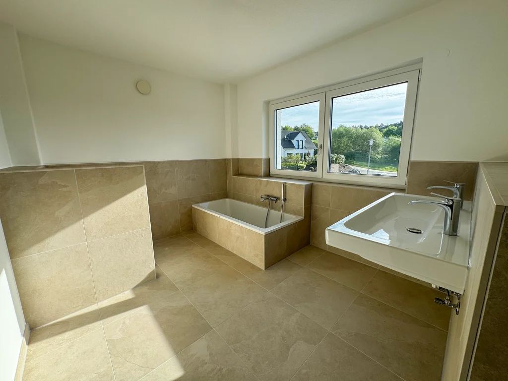 Modernes Badezimmer mit großzügiger Badewanne, bodengleicher Dusche und zeitlosen Fliesen in Natursteinoptik.