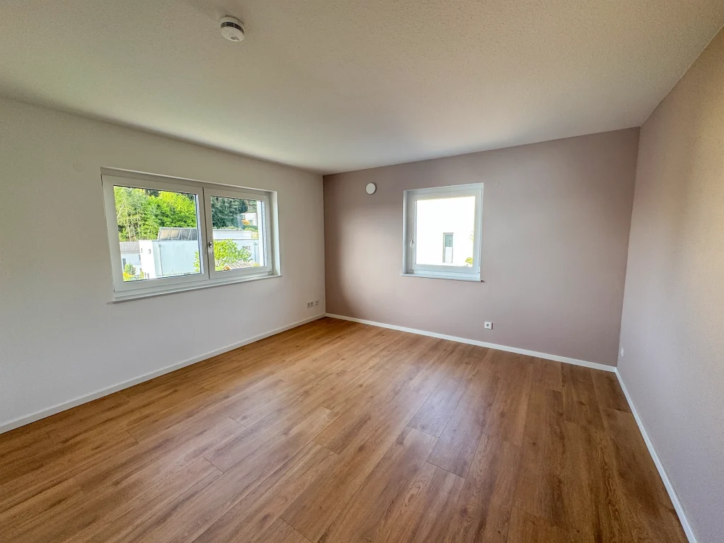 Helles Schlafzimmer mit großzügigen Fensterflächen, warmem Vinylboden in Holzoptik und freundlicher Farbgestaltung.