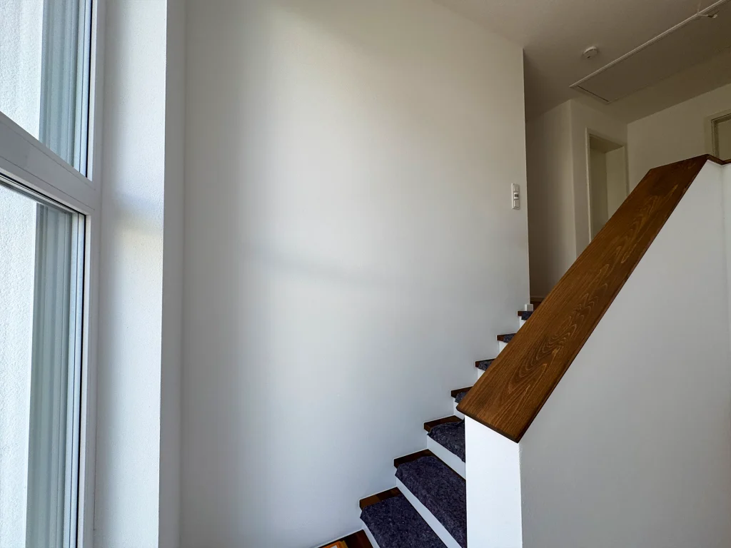 Offener Treppenbereich mit großem Fenster und hochwertigen Holzdetails für ein helles Raumgefühl.
