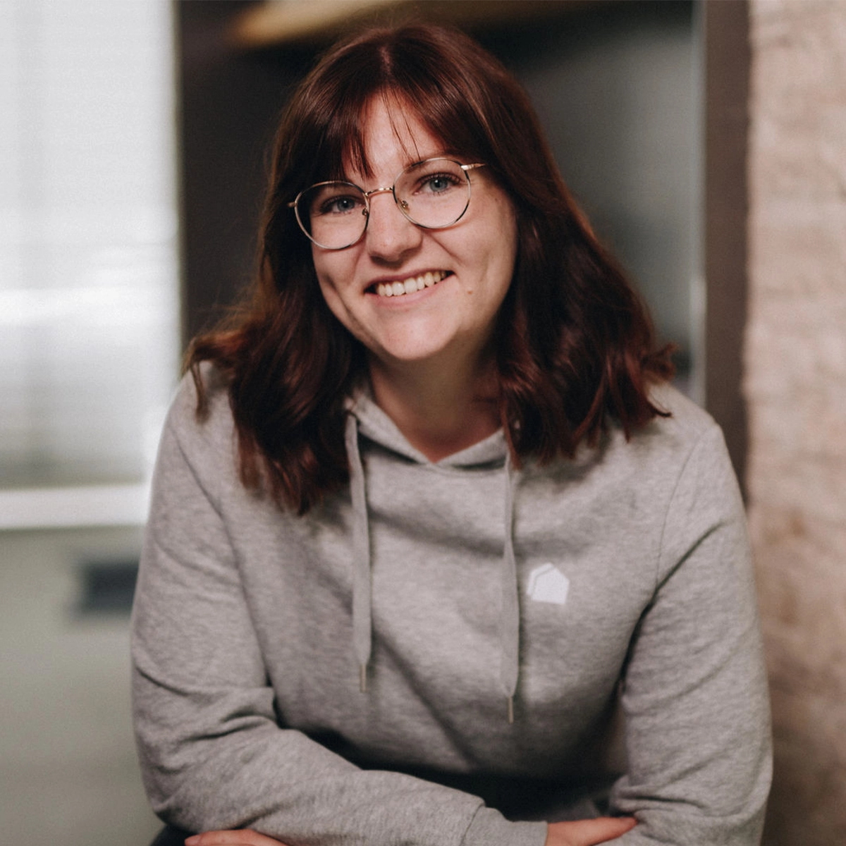 Selina lächelt freundlich in die Kamera und trägt einen grauen Hoodie sowie eine runde Brille.