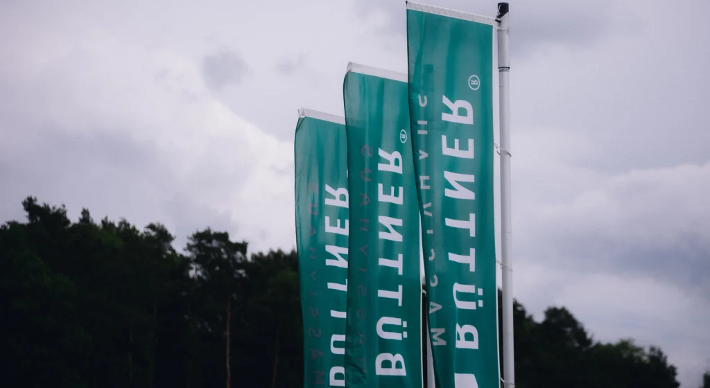 Büttner Massivhaus Fahnen vor bewaldeter Landschaft als weithin sichtbares Markenzeichen des Unternehmensstandorts.
