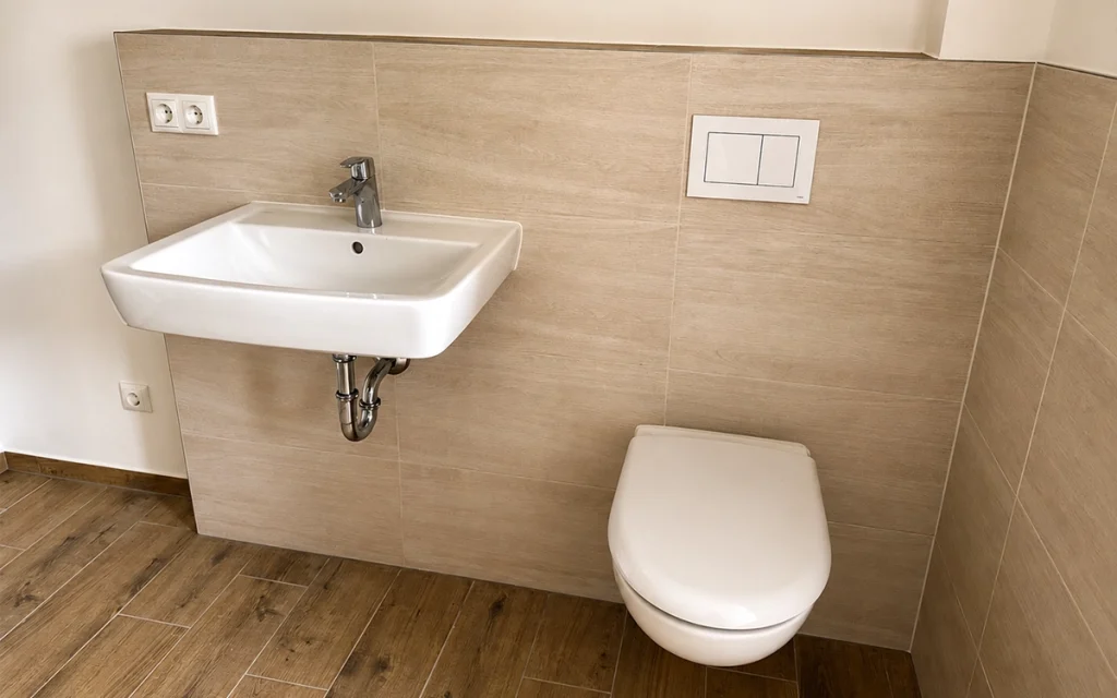 Modernes Badezimmer mit Waschtisch, wandhängendem WC und zeitlosen Fliesen in Holzoptik.