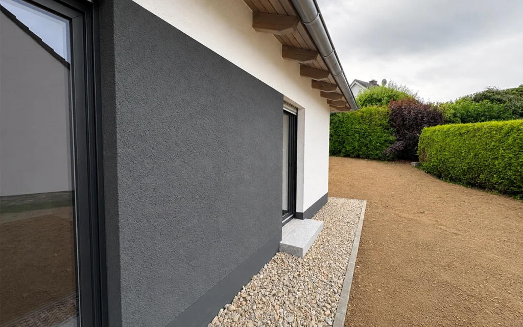 Seitenansicht des modernen Bungalows mit weißer Fassade, anthrazitfarbenen Akzenten und Gartenbereich.
