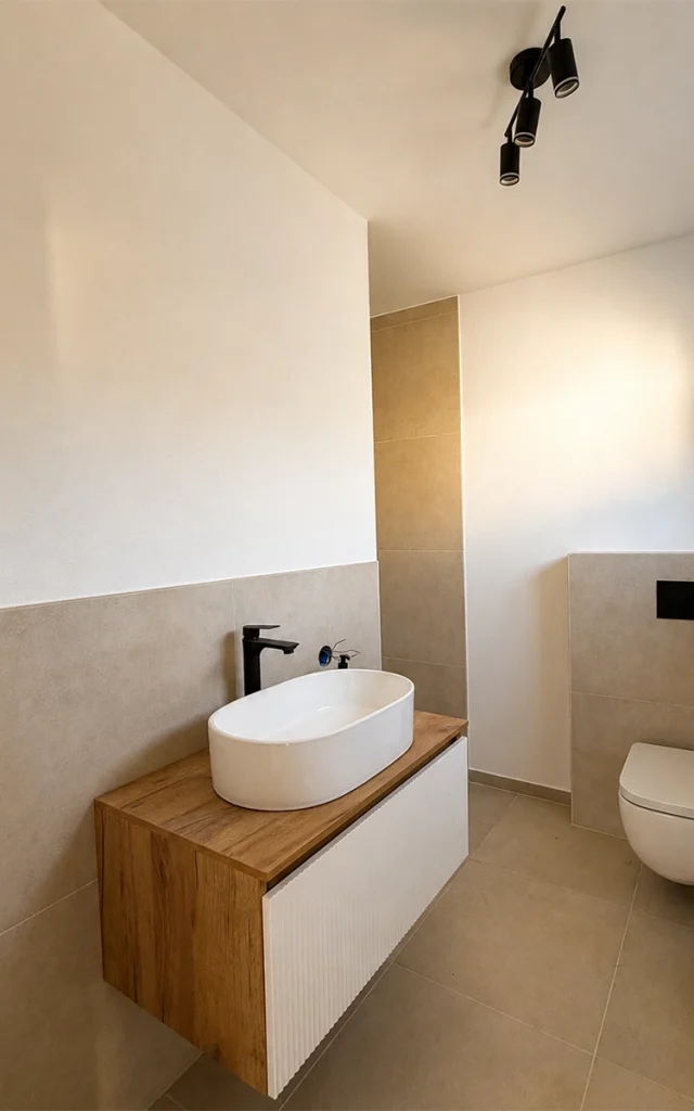 Modernes Badezimmer mit Aufsatzwaschbecken, Waschtisch in Holzoptik, schwarzen Armaturen und wandhängendem WC.
