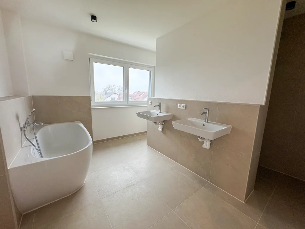 Modernes Badezimmer mit freistehender Badewanne, Doppelwaschbecken und großen Fliesen.